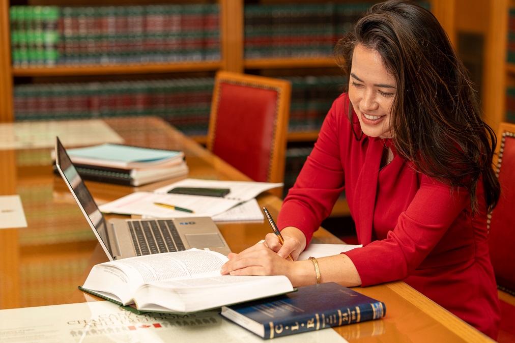 A law clerk working in the library with books and a laptop.