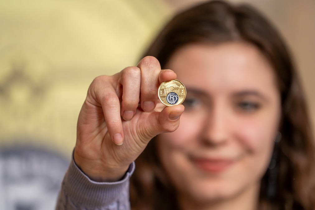 L’artiste qui a conçu le logo du 150e anniversaire de la Cour tient la pièce de 1 $
