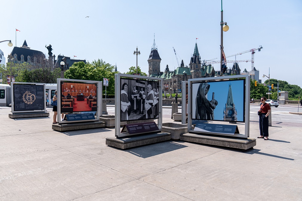 Gros plan de l’exposition sur le pont Plaza avec une personne qui regarde les panneaux et la Colline du Parlement dans l’arrière-plan
