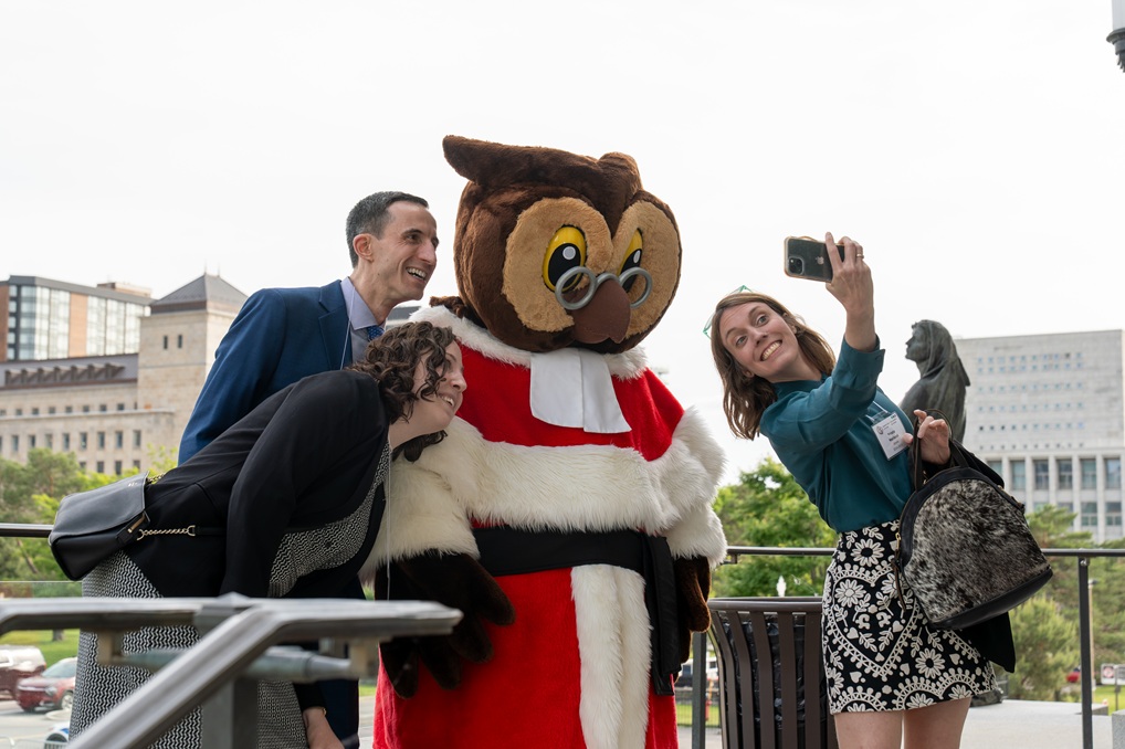 3 participants à la rencontre des auxiliaires juridiques qui prennent une photo d’eux-mêmes avec Amicus, la mascotte de la Cour