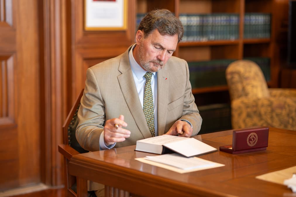 Chief Justice Richard Wagner signs a book while sitting at a table.