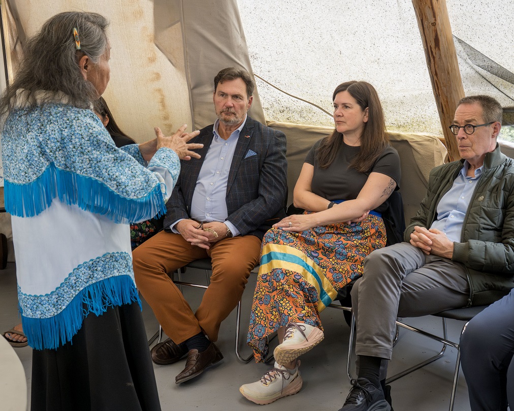 Le juge en chef Wagner et les juges Kasirer et O’Bonsawin écoutent une Aînée parler dans une tente.