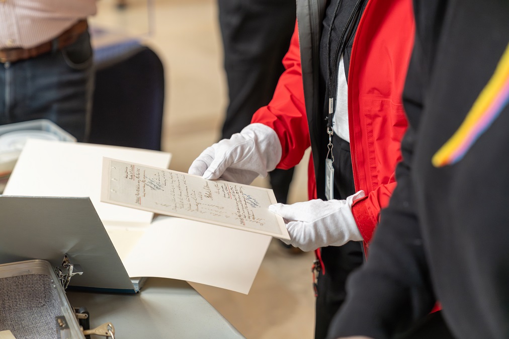 Une personne portant des gants blancs manipule des documents d’archives