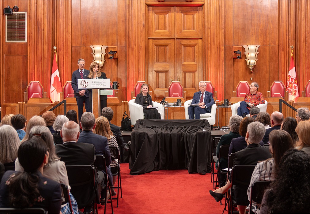 Les juges Karakatsanis et Kasirer parle à partir d’un podium dans la salle d’audience principale, alors que des panélistes attendent sur une scène