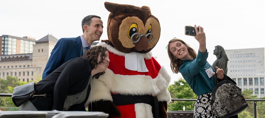 3 personnes se prennent en photo avec Amicus, la mascotte de la Cour suprême